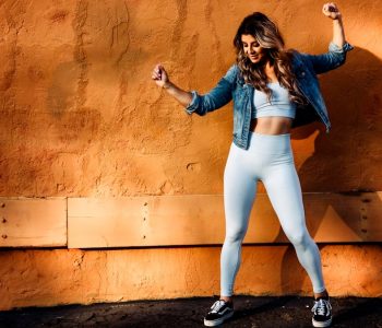 a woman posing in front of a wall with her arms in the air