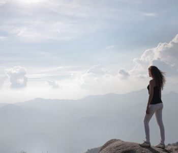 A woman standing on a mountain cliff, enjoying the sunrise and panoramic views.