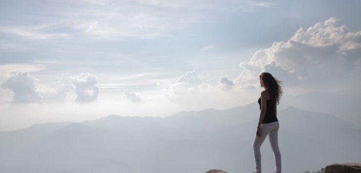 A woman standing on a mountain cliff, enjoying the sunrise and panoramic views.
